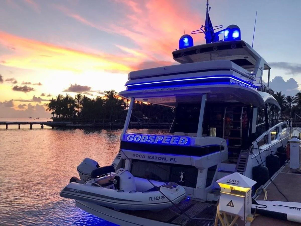 A luxurious yacht is docked at sunset, showcasing its sleek design and vibrant blue lighting. aboard GODSPEED Yacht for Sale