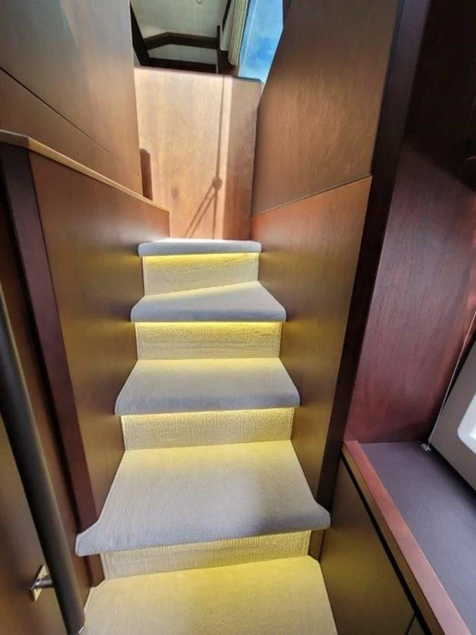 A well-lit staircase with wooden paneling and carpeted steps leads to the upper deck. aboard GODSPEED Yacht for Sale
