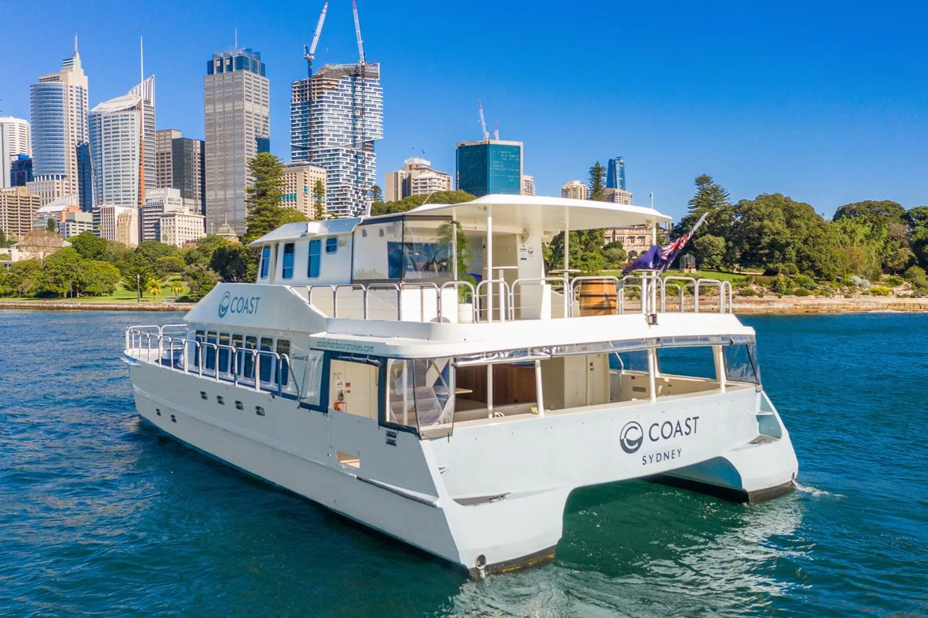 A modern yacht is cruising in a scenic harbor with a city skyline in the background. aboard COAST Yacht for Sale