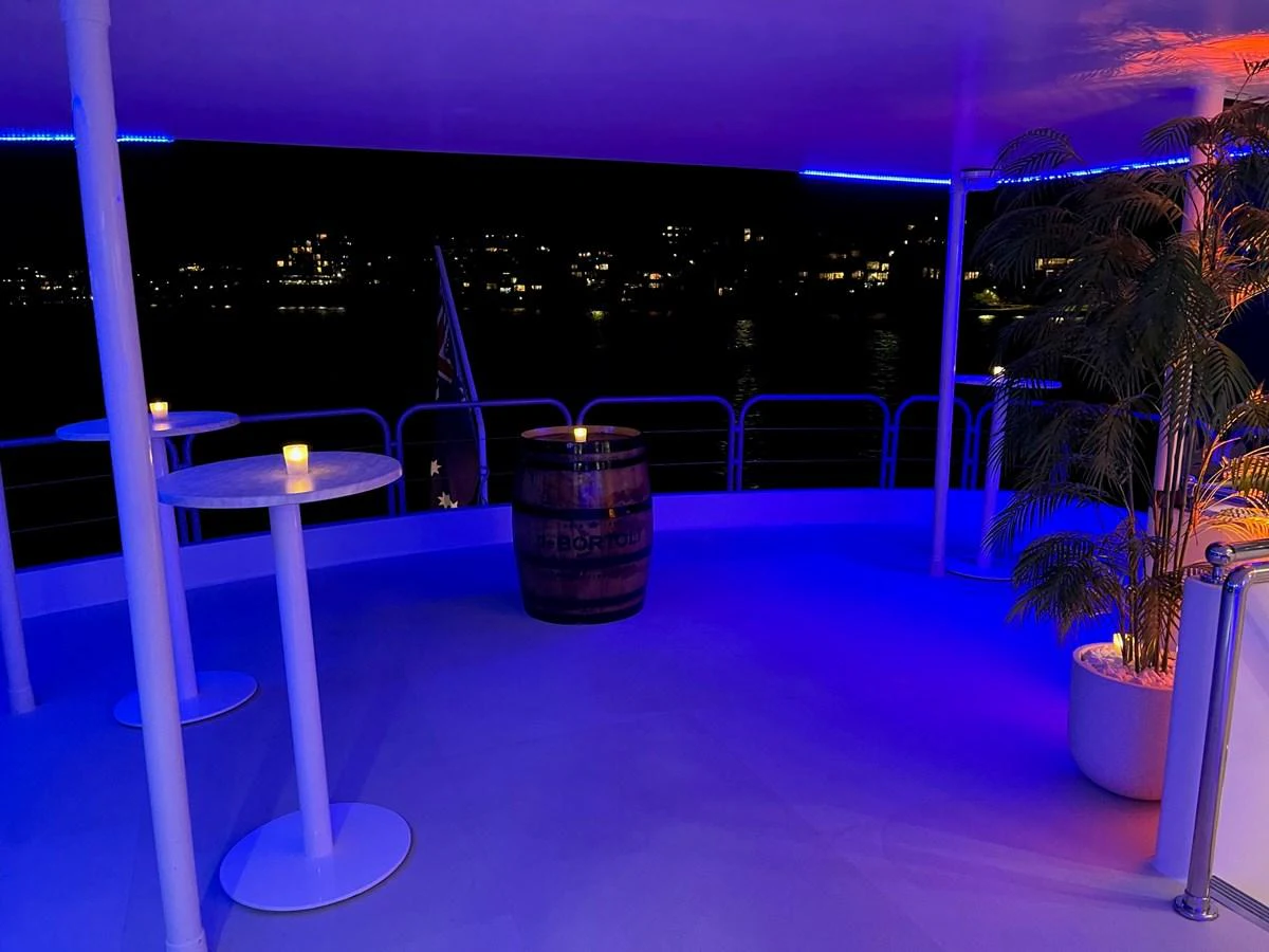 An inviting deck area illuminated with blue lighting, featuring a barrel table and potted plants, perfect for evening relaxation. aboard COAST Yacht for Sale