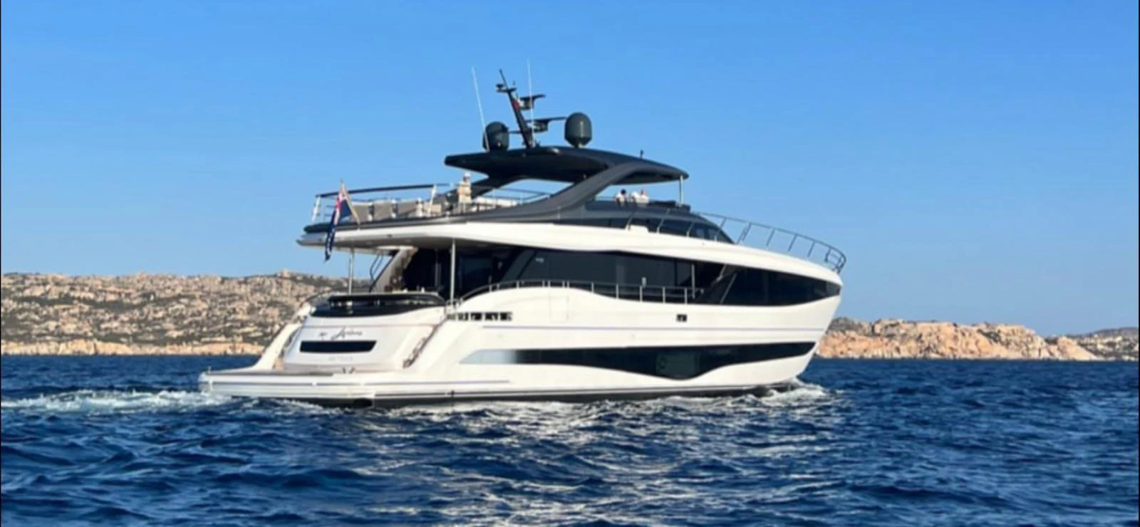 A sleek and modern yacht cruising on the open water with a scenic rocky coastline in the background. aboard LEILANI Yacht for Sale