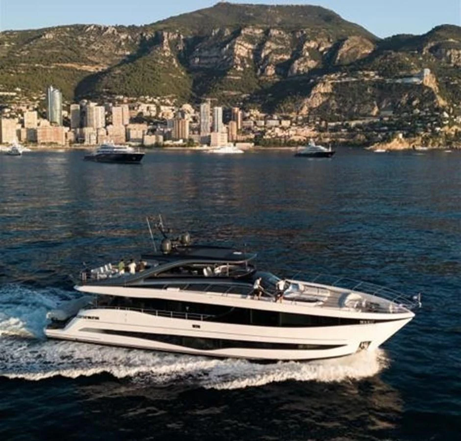 A sleek yacht cruises along the coastline with a stunning cityscape and mountainous backdrop. aboard LEILANI Yacht for Sale