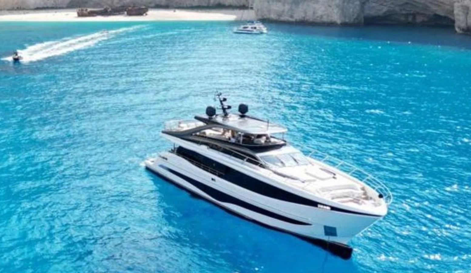 A sleek yacht glides through crystal-clear blue waters near a rocky coastline. aboard LEILANI Yacht for Sale