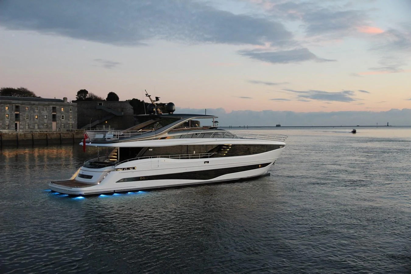 A sleek and modern yacht cruises gracefully on calm waters at dusk, illuminated by underwater lights. aboard LEILANI Yacht for Sale