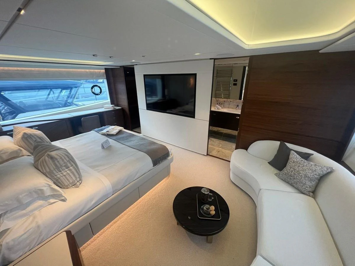The master stateroom features a luxurious bed, a cozy seating area, and a large flat-screen TV, all bathed in natural light. aboard LEILANI Yacht for Sale