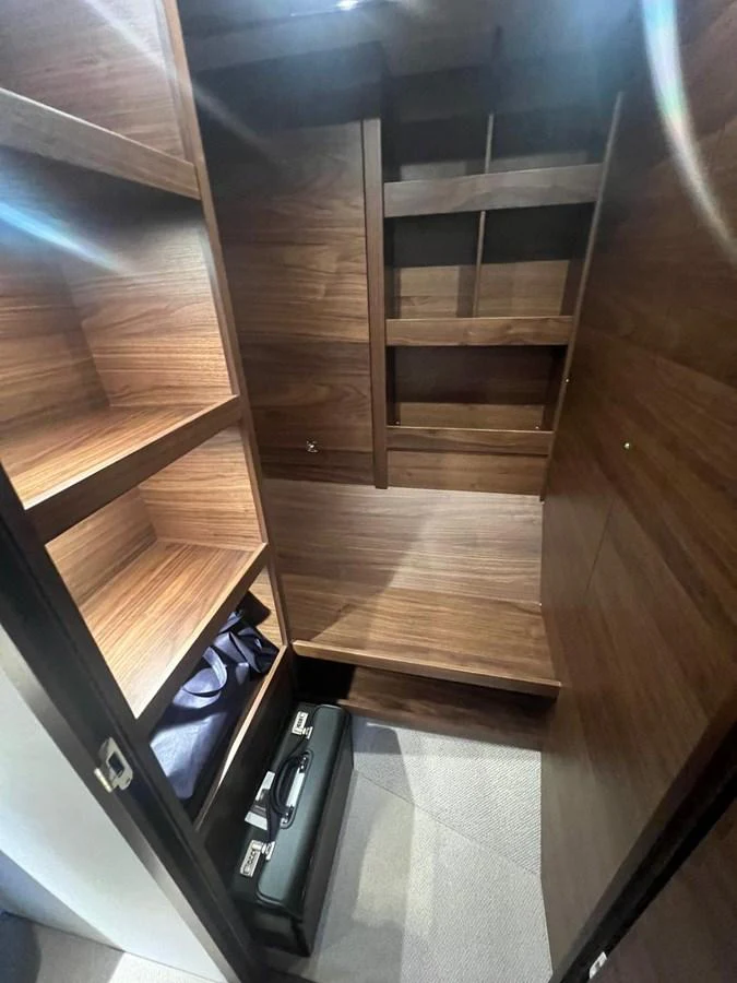 A compact and well-organized storage area with wooden shelves and a suitcase. aboard LEILANI Yacht for Sale