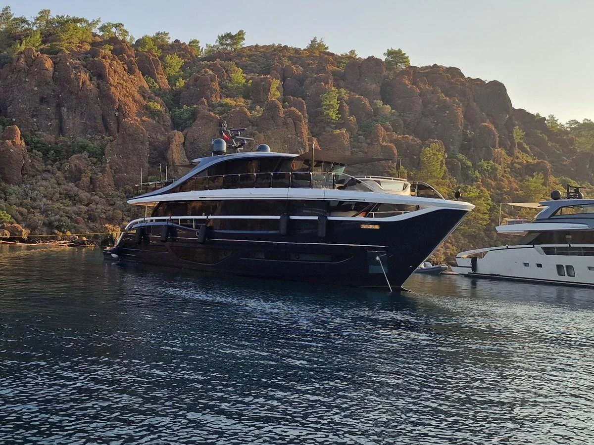 A sleek and modern yacht is anchored in a serene bay, surrounded by rocky cliffs and lush greenery. aboard OCEAN THREE Yacht for Sale