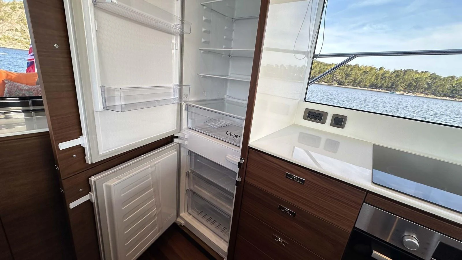 The galley features a modern refrigerator and ample storage space, with a scenic view through the window. aboard PRINCESS F65 Yacht for Sale