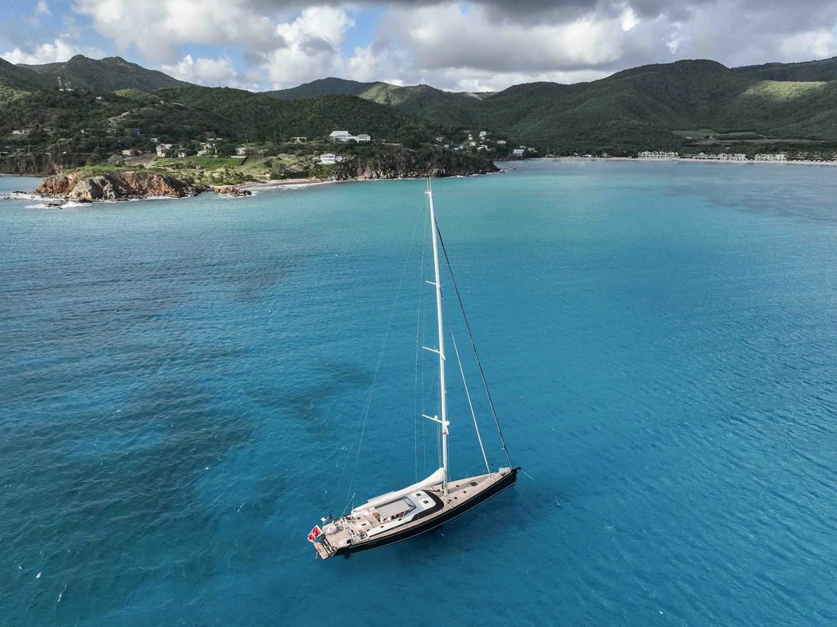 A sleek sailing yacht glides gracefully on tranquil blue waters with a scenic coastline in the background. aboard BLACK PEARL II Yacht for Sale