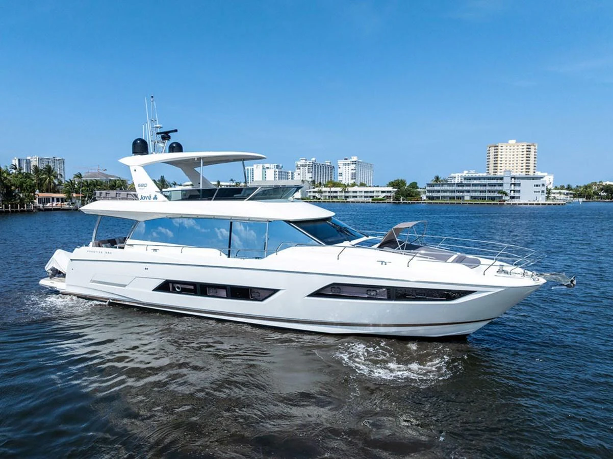 A sleek, modern yacht cruises through calm waters with a cityscape in the background. aboard JOVE Yacht for Sale
