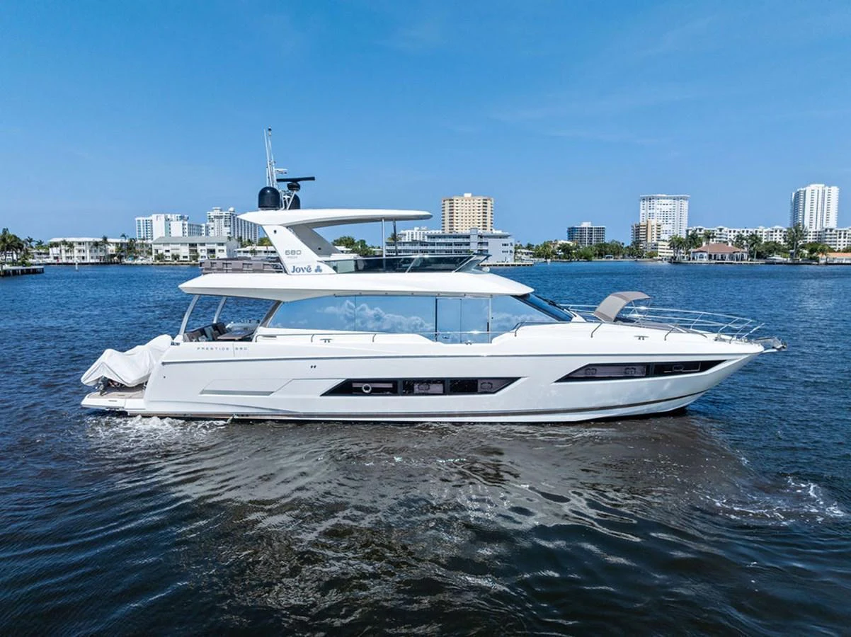 A sleek and modern yacht glides gracefully on calm waters with a cityscape in the background. aboard JOVE Yacht for Sale