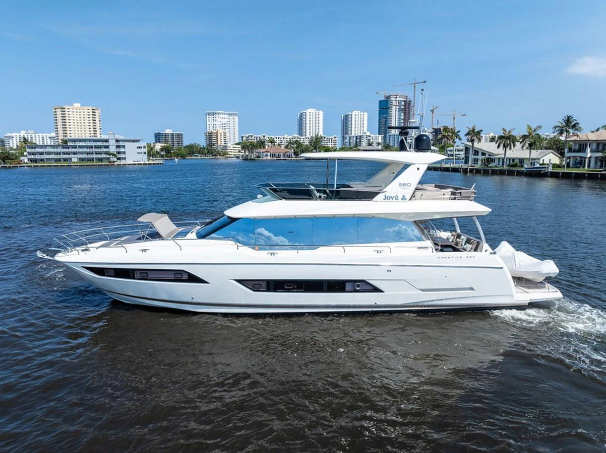 A sleek and modern yacht cruises gracefully on the water with a cityscape in the background. aboard JOVE Yacht for Sale
