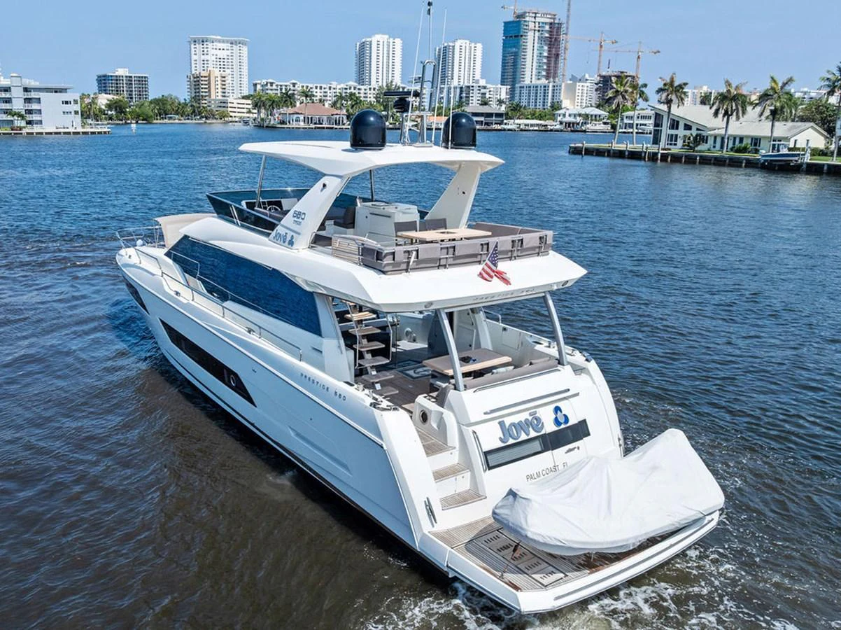 A sleek and modern yacht cruising on calm waters with a cityscape in the background. aboard JOVE Yacht for Sale