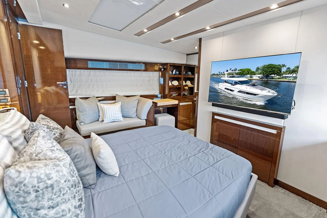 The stateroom features a comfortable bed, a cozy seating area, and a large TV displaying a yacht on the water. aboard JOVE Yacht for Sale