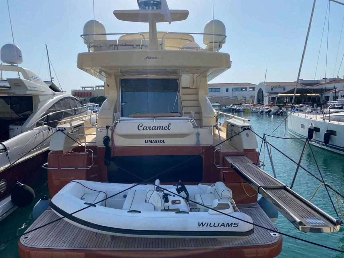 The yacht's stern is showcased, featuring a tender on the swim platform and docked in a marina. aboard CARAMEL Yacht for Sale