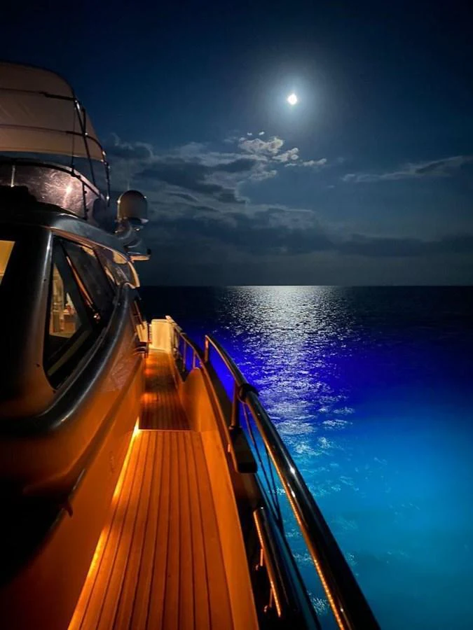 A serene night view of a yacht's deck illuminated by soft lighting, with the moon reflecting on the calm sea. aboard CARAMEL Yacht for Sale