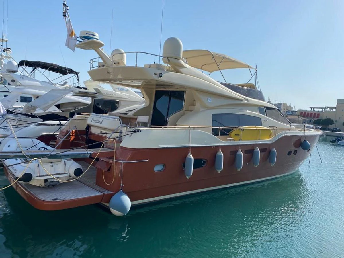 This yacht features a sleek exterior design with a rich brown hull and cream superstructure, docked in a serene marina. aboard CARAMEL Yacht for Sale