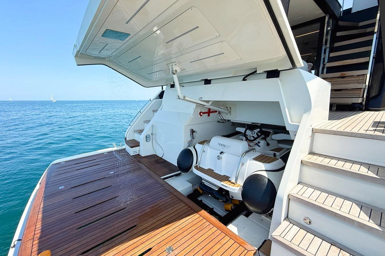 The yacht's garage is open, revealing a neatly stored tender and equipment, with a view of the sea in the background. aboard AMY Yacht for Sale