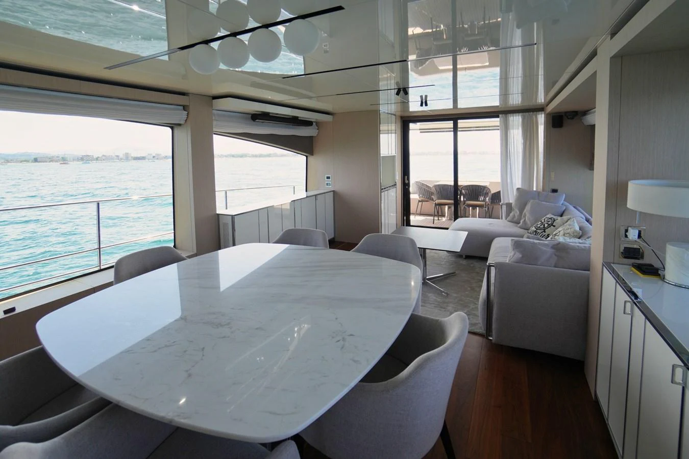 The yacht's salon features a modern dining area with a marble table and comfortable seating, complemented by a lounge area with a view of the sea. aboard AMY Yacht for Sale
