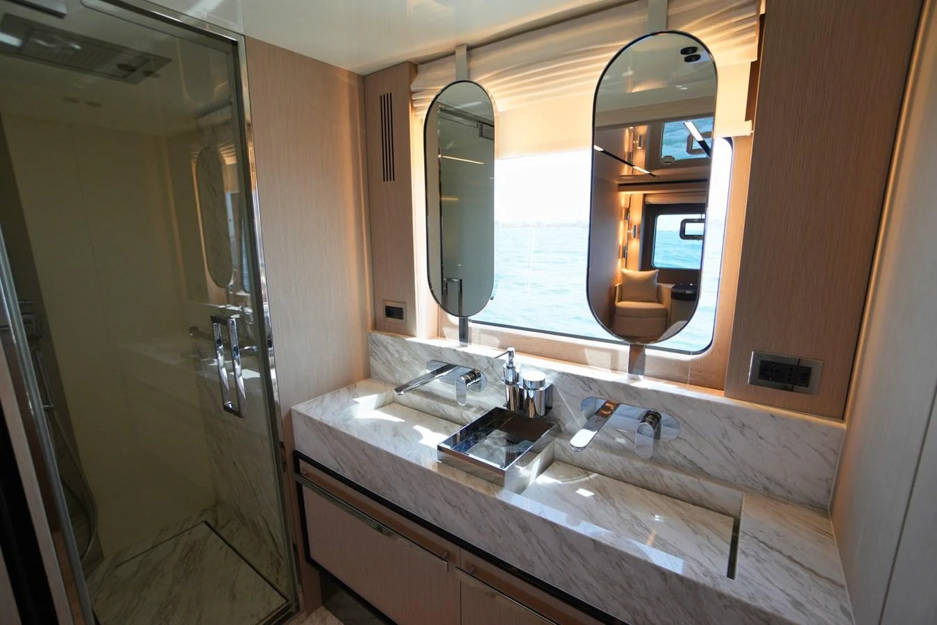 The yacht's bathroom features a sleek design with dual sinks and a large mirror, complemented by a view of the sea through the window. aboard AMY Yacht for Sale