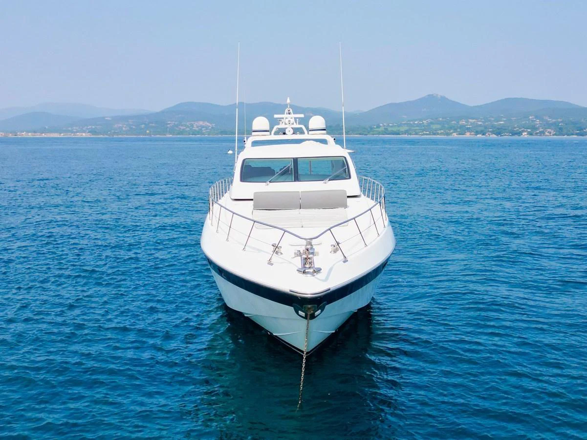 A sleek yacht is anchored on calm blue waters with a scenic coastline in the background. aboard CARO Yacht for Sale