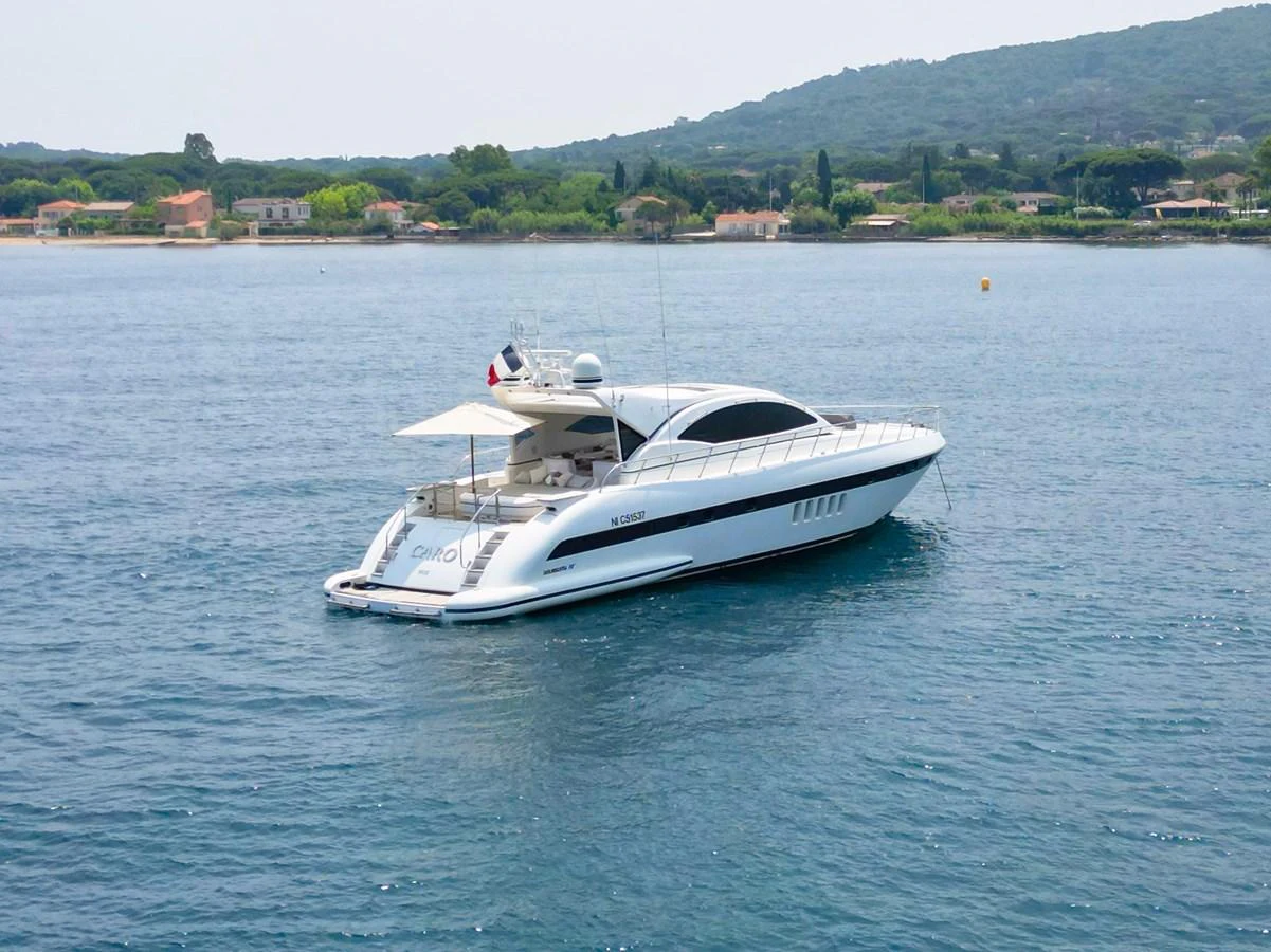 A sleek and modern yacht is anchored in calm waters with a scenic backdrop. aboard CARO Yacht for Sale