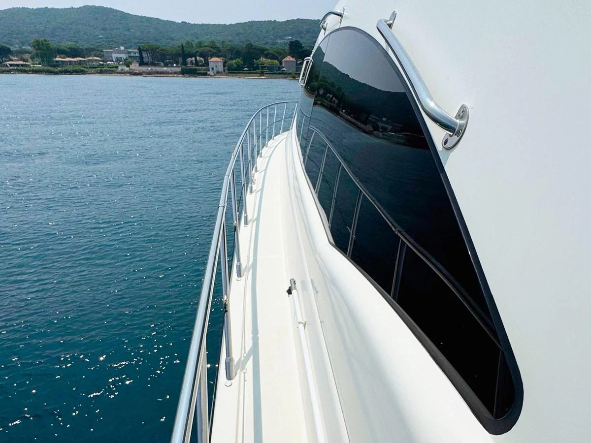 A sleek yacht cruising on calm waters with a scenic shoreline in the background. aboard CARO Yacht for Sale