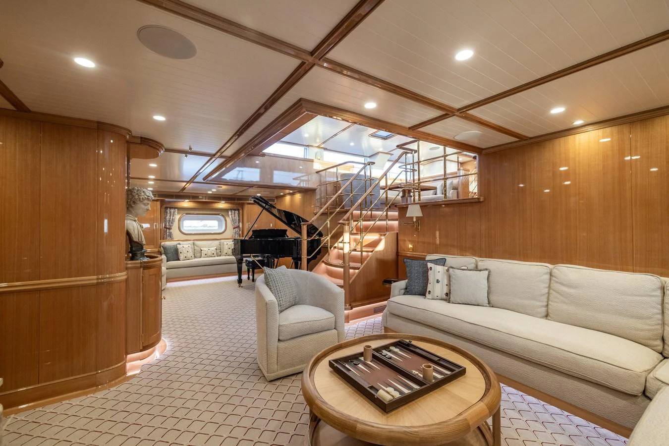 The salon features elegant wood paneling, plush seating, and a grand piano, creating a sophisticated ambiance. aboard MAXIMUS Yacht for Sale