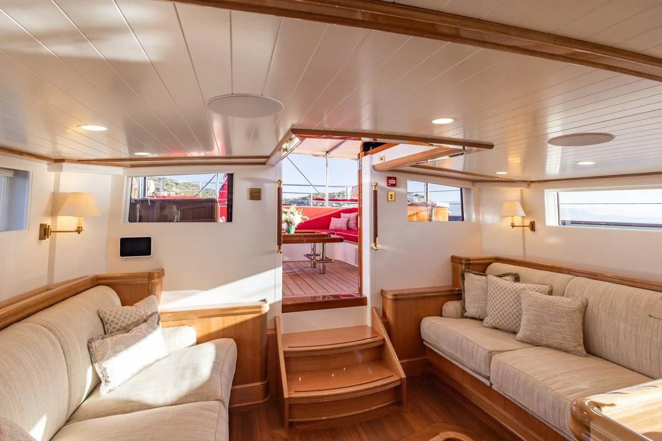 The cozy interior seating area features plush sofas and warm wooden accents, leading to an outdoor deck. aboard MAXIMUS Yacht for Sale