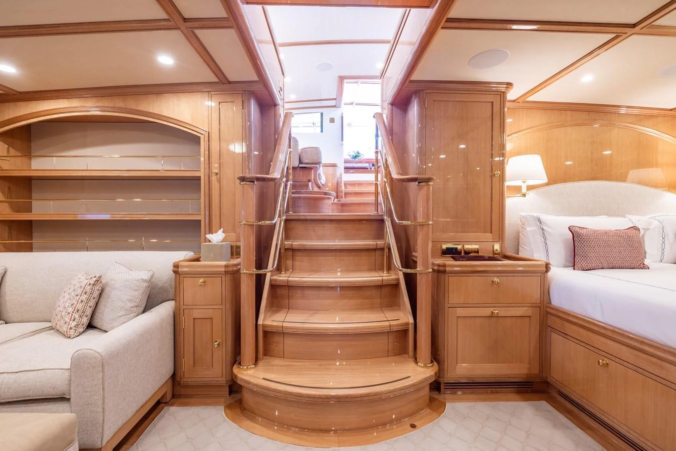 The yacht's interior features a beautifully crafted wooden staircase leading to an upper level, surrounded by elegant furnishings and soft lighting. aboard MAXIMUS Yacht for Sale