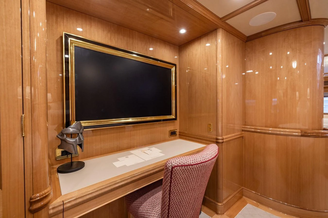 The yacht's office features a sleek desk, a comfortable chair, and a large wall-mounted TV, all set within a polished wood-paneled room. aboard MAXIMUS Yacht for Sale