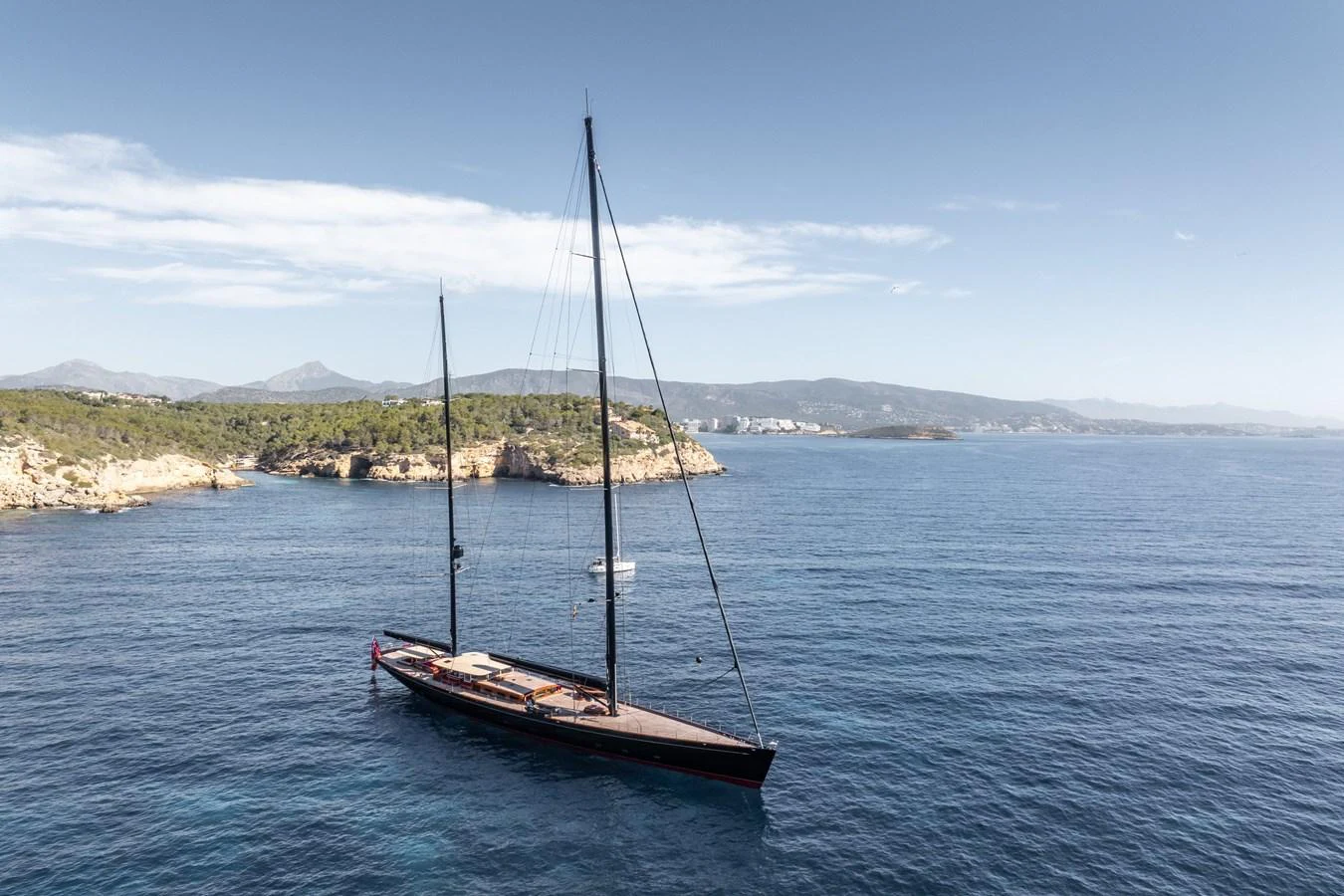A sleek sailing yacht glides gracefully on calm blue waters near a scenic coastline. aboard MAXIMUS Yacht for Sale