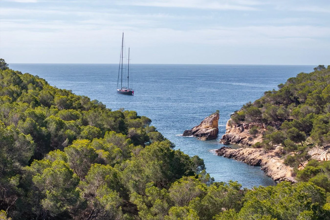 A serene view of a yacht anchored in a secluded cove surrounded by lush greenery. aboard MAXIMUS Yacht for Sale