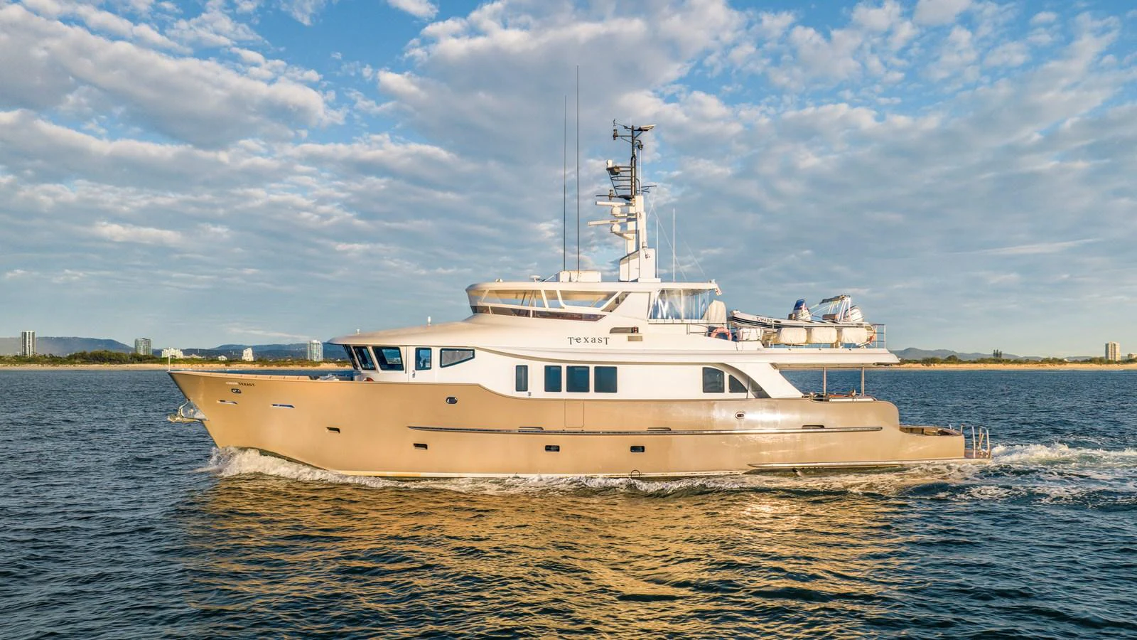 A luxurious yacht cruises smoothly on calm waters under a partly cloudy sky. aboard TEXAS T Yacht for Sale