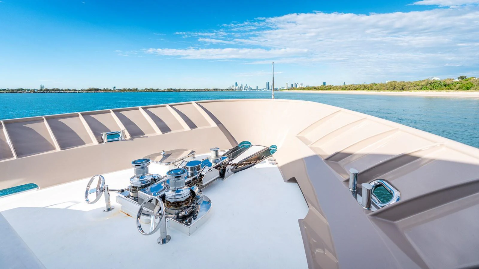 The bow of the yacht features a clean and well-maintained anchor winch system with a scenic coastal backdrop. aboard TEXAS T Yacht for Sale
