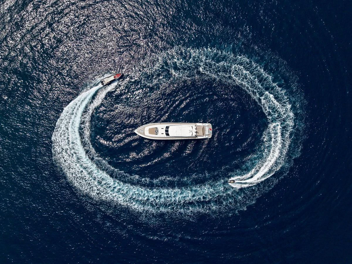 Aerial view of a yacht cruising in the ocean with two smaller boats creating a circular wake around it. aboard CHEEKY TIGER Yacht for Sale