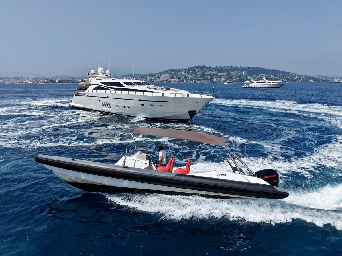 A sleek yacht cruises through the blue waters, accompanied by a smaller tender boat in the foreground. aboard CHEEKY TIGER Yacht for Sale