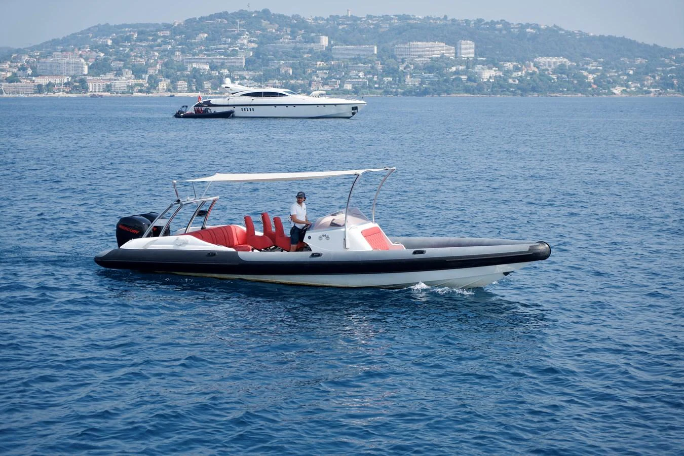 A sleek tender with a white canopy and red seating glides on calm waters with a scenic coastal backdrop. aboard CHEEKY TIGER Yacht for Sale