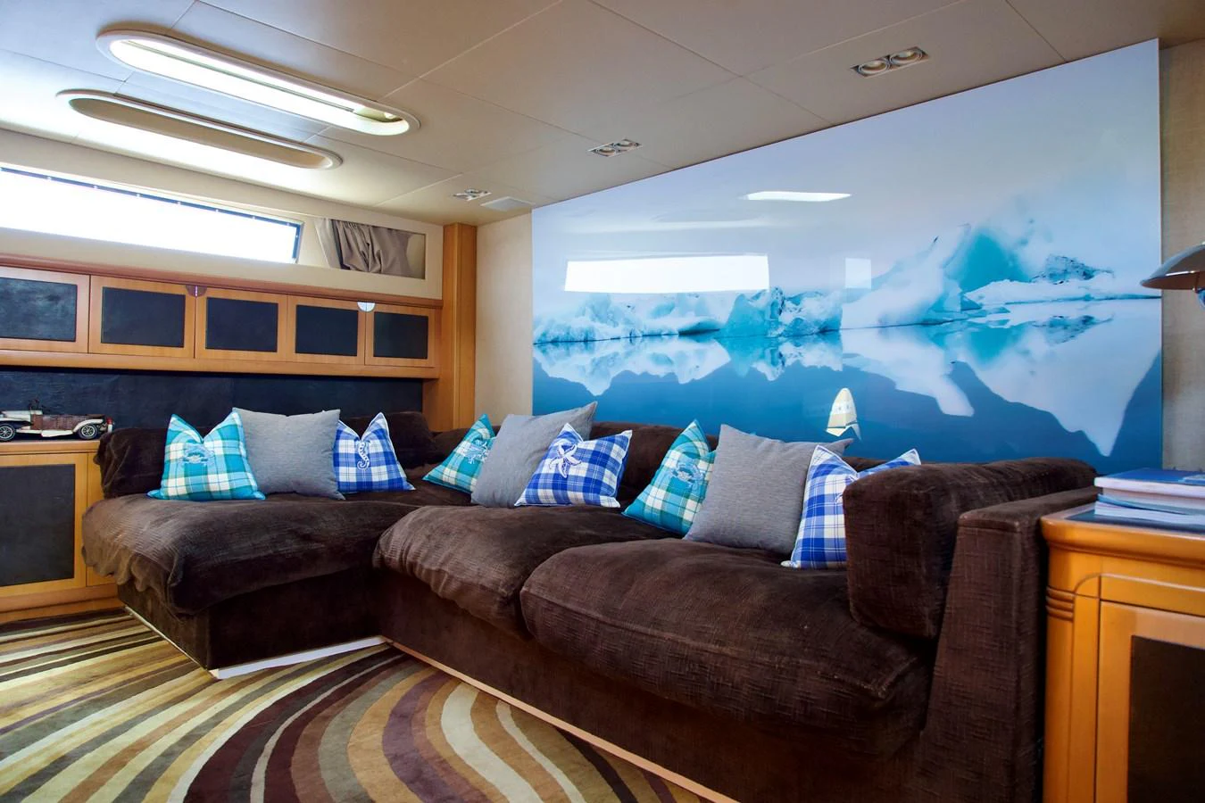 The yacht's salon features a cozy seating area with plush brown sofas and vibrant blue pillows, complemented by a stunning wall mural of icy landscapes. aboard CHEEKY TIGER Yacht for Sale