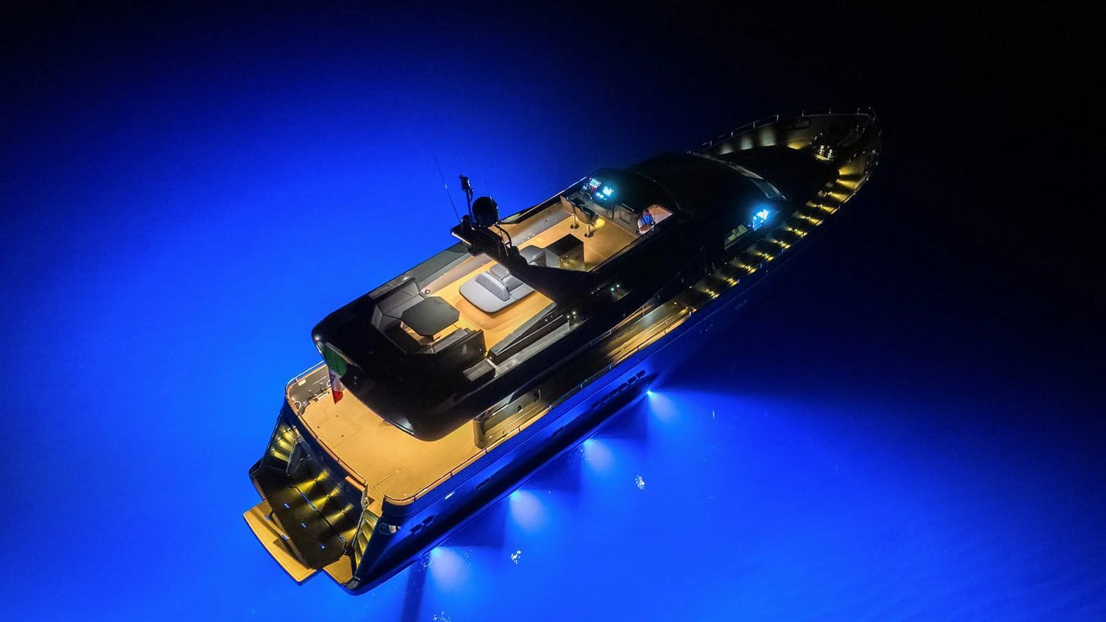 A sleek yacht illuminated by vibrant blue underwater lights, creating a striking night-time ambiance. aboard MAVERICK Yacht for Sale