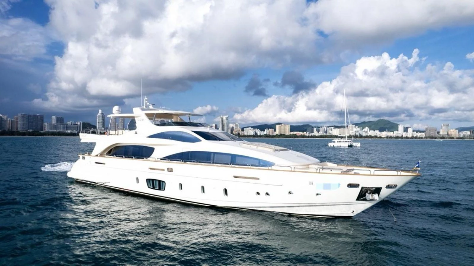 A sleek white yacht cruises gracefully on the water with a cityscape in the background. aboard AZIMUT 105 Yacht for Sale