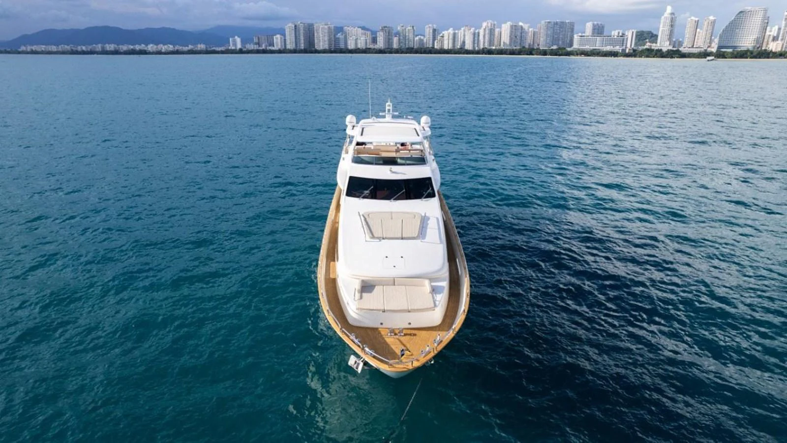 A luxurious yacht is anchored in calm waters with a cityscape in the background. aboard AZIMUT 105 Yacht for Sale