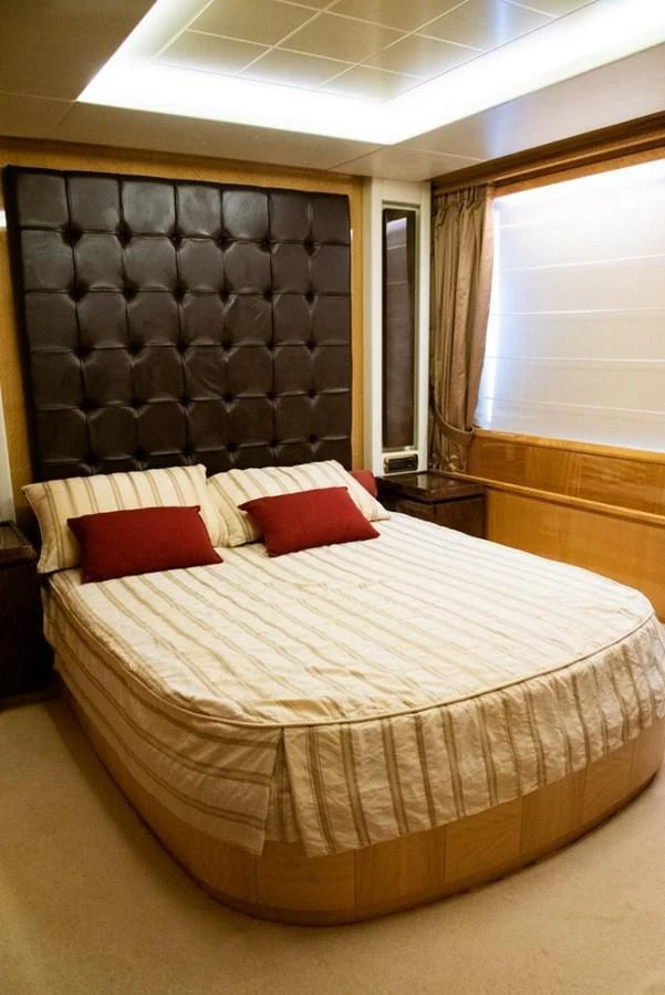 The stateroom features a comfortable bed with striped linens and plush pillows, set against a tufted headboard. aboard AZIMUT 105 Yacht for Sale
