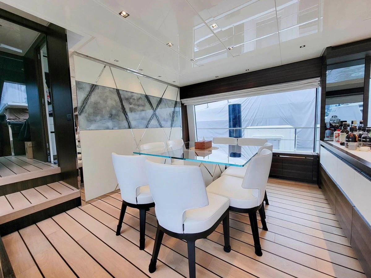 The yacht's dining area features a sleek glass table surrounded by modern white chairs, set against a backdrop of large windows and contemporary decor. aboard SANLORENZO SL86 Yacht for Sale