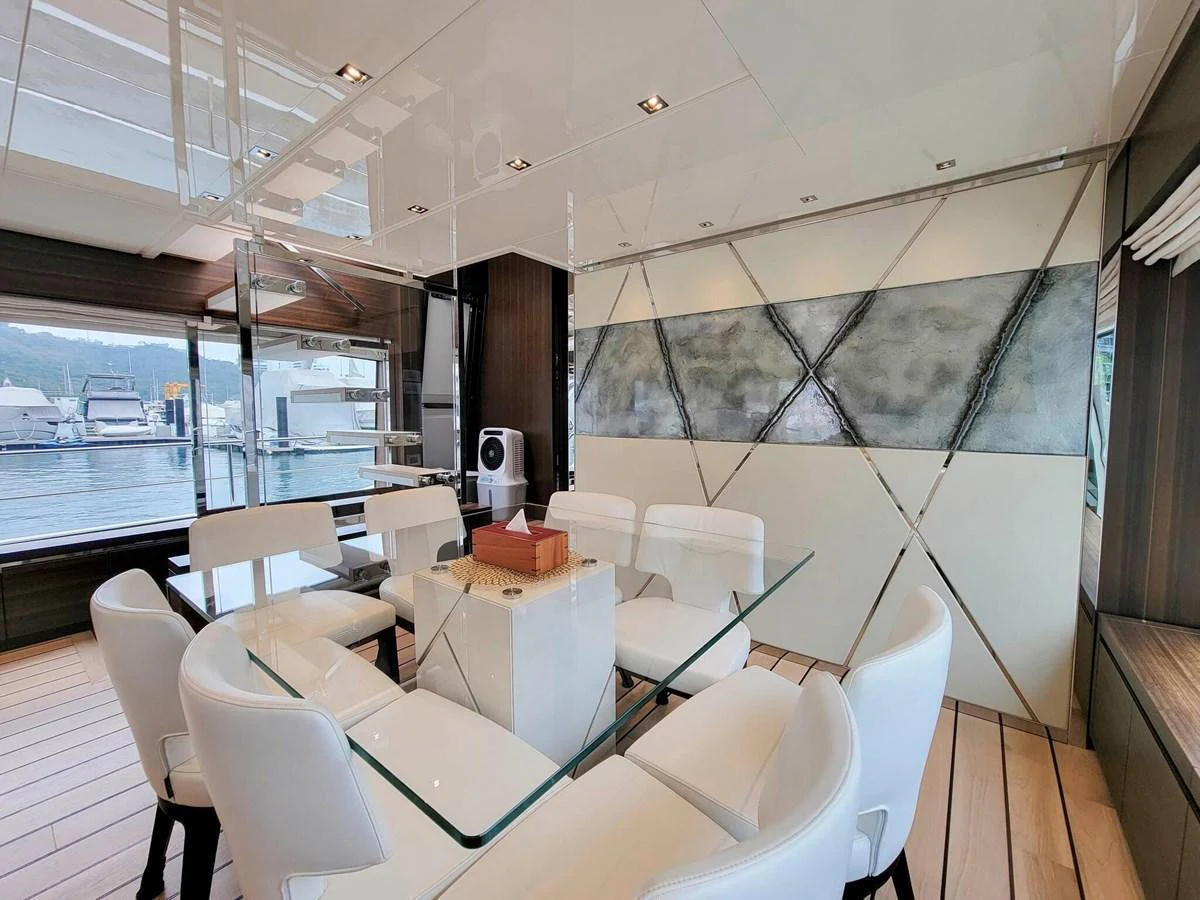 The yacht's dining area features a modern glass table surrounded by plush white chairs, set against a backdrop of large windows offering a scenic view. aboard SANLORENZO SL86 Yacht for Sale
