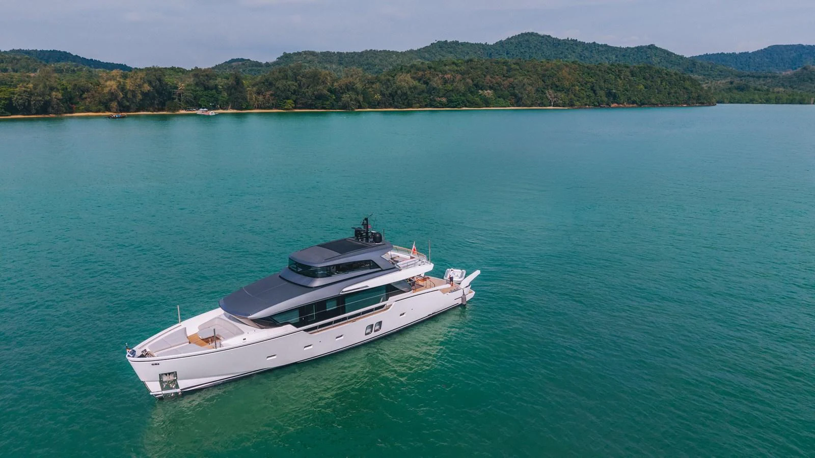 A sleek and modern yacht cruising in tranquil turquoise waters with a lush green shoreline in the background. aboard SANLORENZO SX88 Yacht for Sale