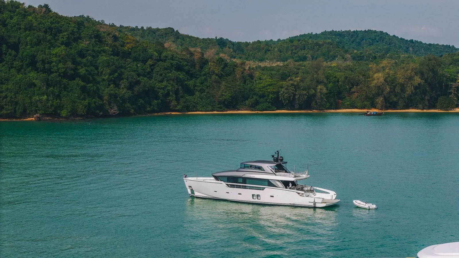 A sleek yacht is anchored in a serene bay surrounded by lush greenery. aboard SANLORENZO SX88 Yacht for Sale