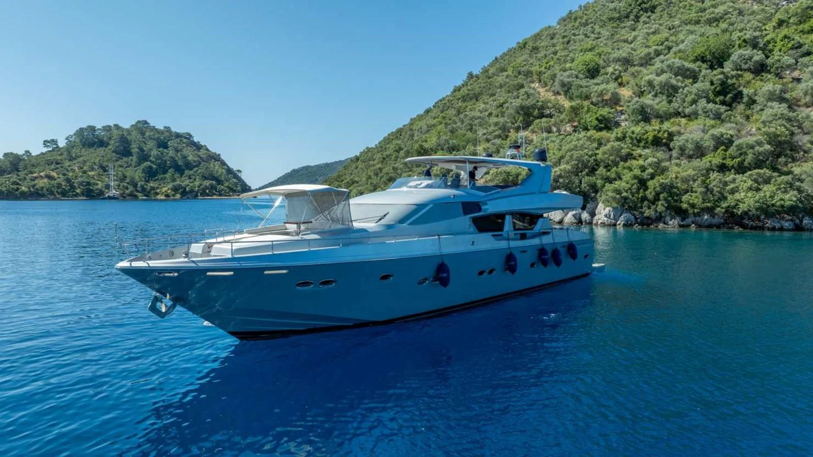 A sleek yacht glides through tranquil blue waters against a backdrop of lush green hills. aboard SILVER Yacht for Sale