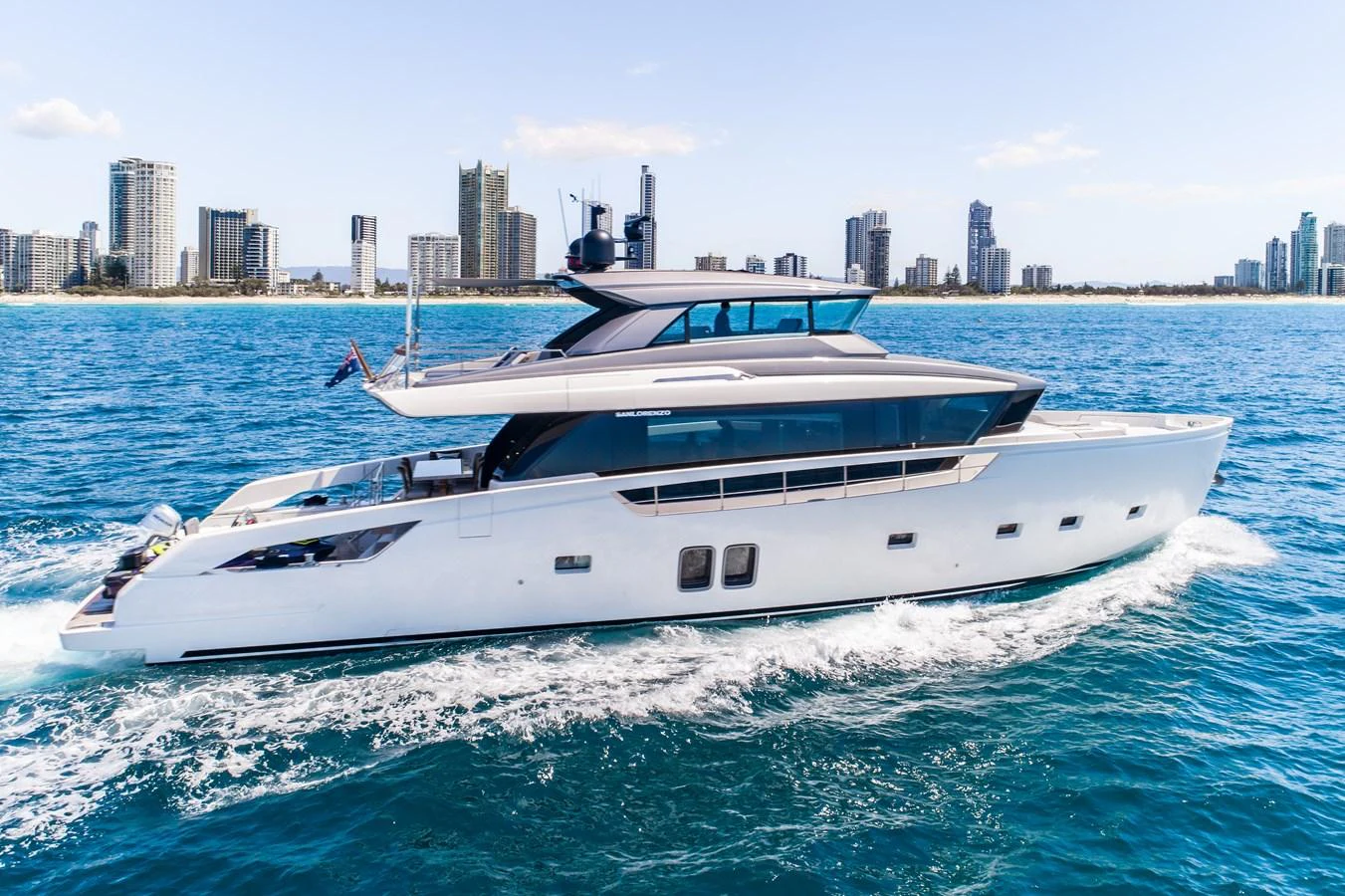 A sleek and modern yacht cruises through the water with a city skyline in the background. aboard VIOLETTA Yacht for Sale