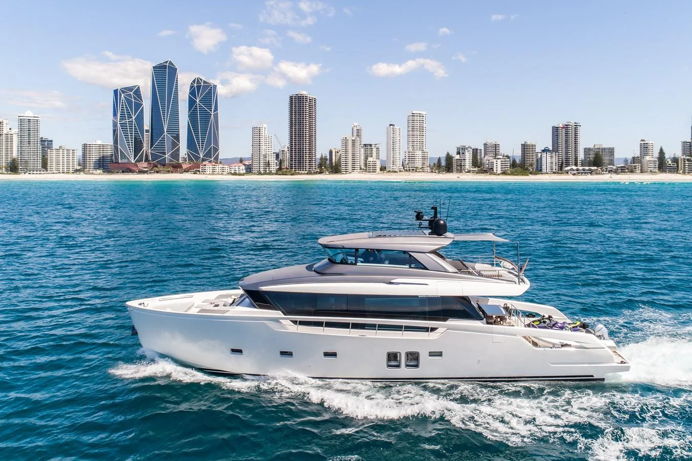 A sleek and modern yacht cruises along the coastline with a cityscape in the background. aboard VIOLETTA Yacht for Sale